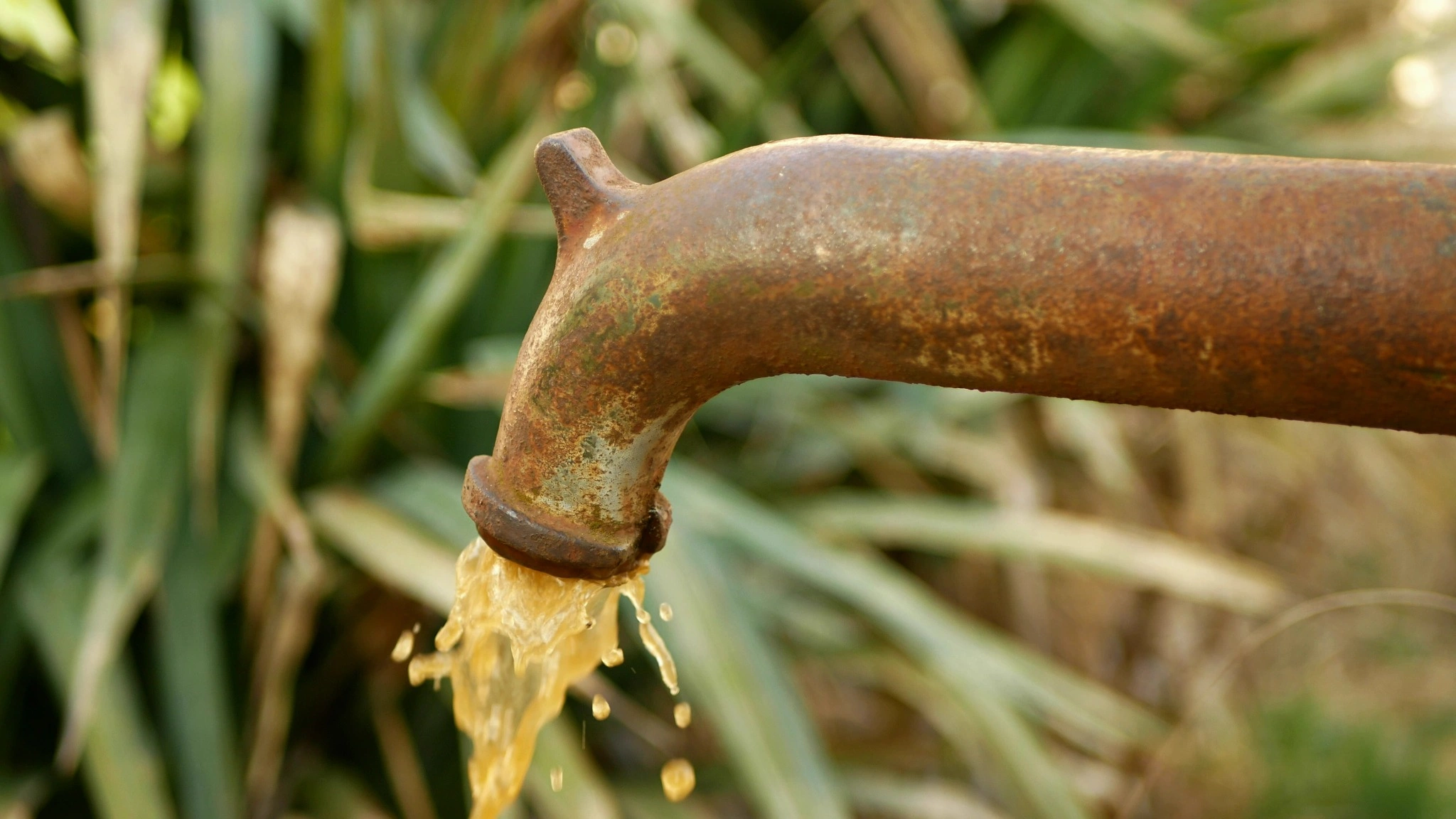 Rusty outdoor water pipe releasing discolored water, illustrating signs of contaminated well water in New Hampshire