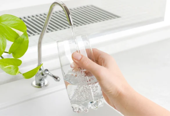 Glass of filtered water being filled from a modern kitchen faucet